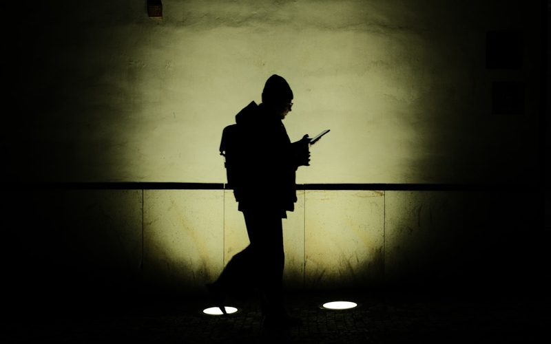 Silhouette of a person walking alone at night while checking their phone